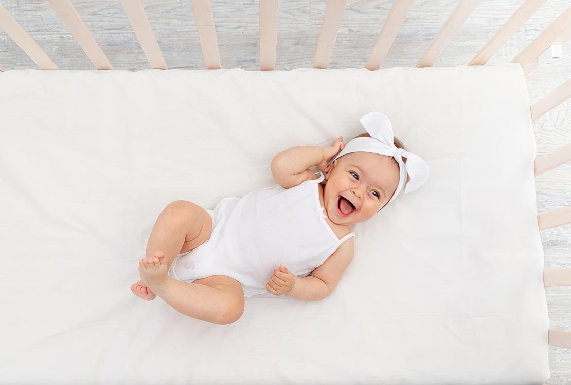 A smiling baby laying in a crib set up for safe sleep
