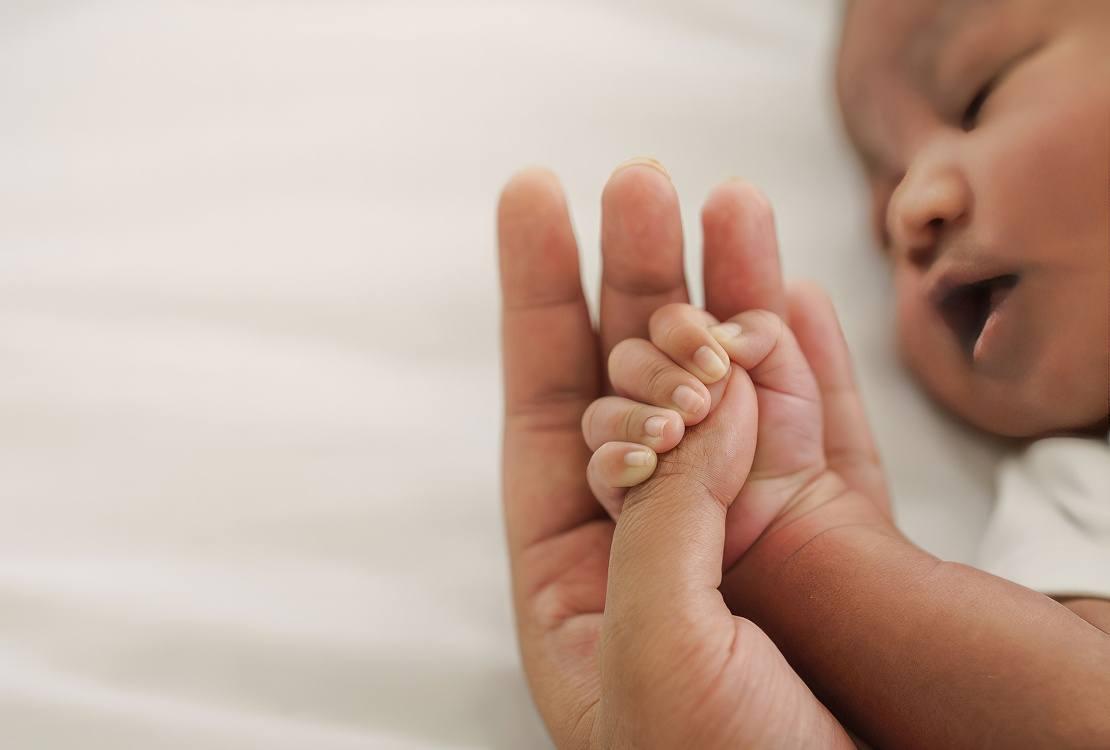 Infant holding parent’s thumb
